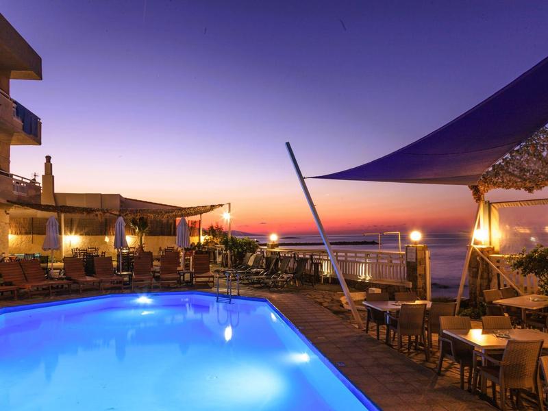 Abendliche Aufnahme eines beleuchteten Pools und einer Terrasse mit Tischen und Stühlen in einem Hotel.