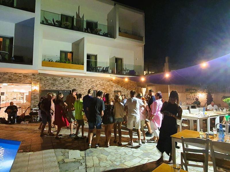 Menschen feiern nachts am Pool und Terrasse eines Hauses mit Balkon und Beleuchtung.