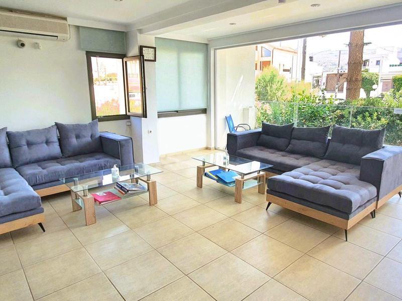 Helles Wohnzimmer mit grauen Sofas, Fliesenboden und großem Fenster zur Terrasse mit Pflanzen.