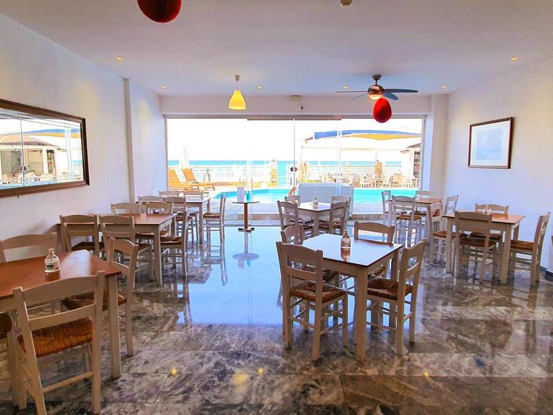 Leerer Gastraum mit Holztischen und Stühlen, großer Spiegel an der Wand, helle Deckenlampen.