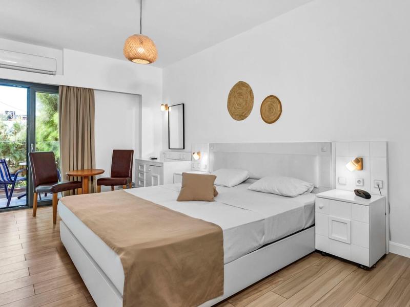Modernes Hotelzimmer mit Doppelbett, Balkon und gemütlicher Einrichtung in hellen Farben.
