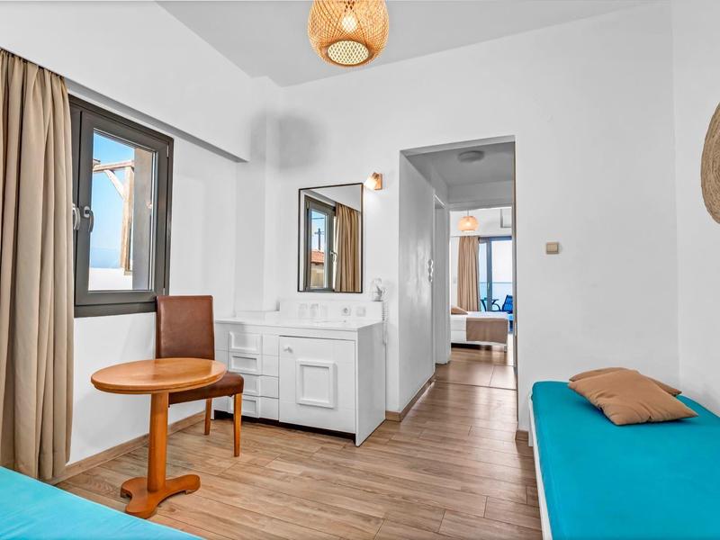 Helles Hotelzimmer mit zwei Betten, Holzboden und Blick auf ein angrenzendes Zimmer.