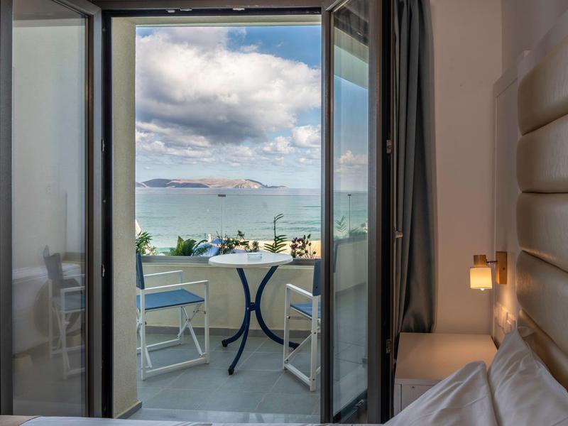 Blick von einem Hotelzimmer auf einen Balkon mit Zwei Stühlen und Meer im Hintergrund.