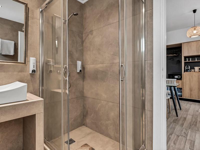 Modernes Badezimmer mit Glasdusche, Waschbecken und Zugang zu einem Wohnzimmerbereich.