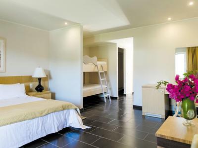 Pokój z łóżkiem podwójnym, łóżkiem piętrowym, lampką nocną i kwiatami na stole.