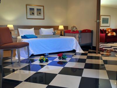 Pokój hotelowy z białym łóżkiem, dwiema lampkami nocnymi i czarno-białą szachownicą na podłodze.