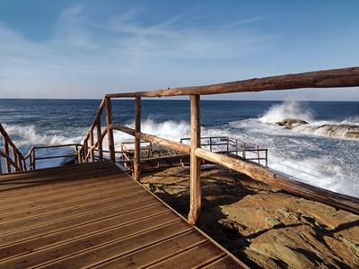 Drewniany taras z balustradą nad skalistym wybrzeżem i burzliwym morzem pod niebieskim niebem