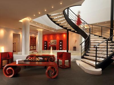 Elegancka lobby hotelowa z zakrzywionymi schodami, czerwonymi meblami i stylowym oświetleniem.