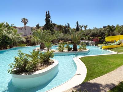 Schwimmbad mit Palmen, Wasserrutschen und gepflegtem Rasen in einer sonnigen Anlage.