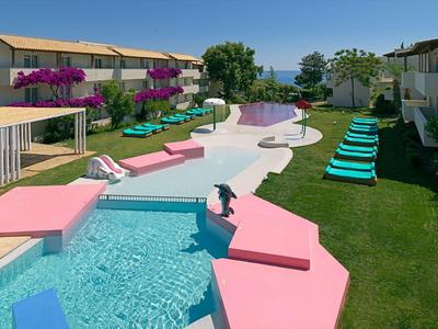 Nowoczesny basen hotelowy z różową obwódką, leżakami i widokiem na morze przy czystym niebie.