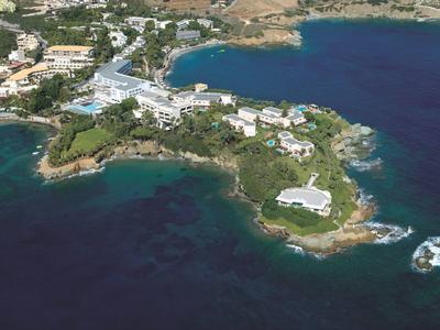 Widok z lotu ptaka na nadmorski ośrodek z kilkoma budynkami na skalistym półwyspie otoczonym błękitnym morzem.