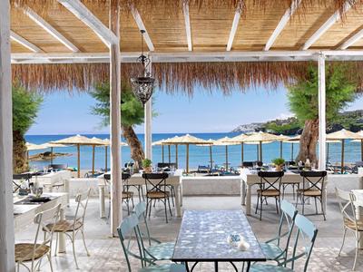 Offener Speisesaal mit Blick auf Strand und Meer, Tische und Stühle unter Holz- und Strohdach.