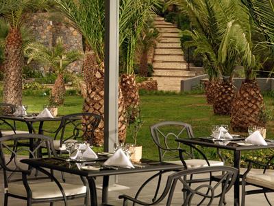 Outdoor-Restaurantbereich mit Eisentischen und Stühlen, umgeben von Palmen und Grünfläche.