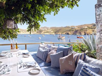 Gemütliche Terrasse mit Polstern, Blick aufs Meer und Boote bei klarem Himmel.