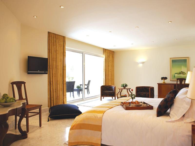 Jasny pokój hotelowy z podwójnym łóżkiem, żółtymi zasłonami i balkonem z krzesłami.