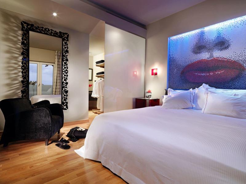 Nowoczesny pokój hotelowy z dużym łóżkiem, czarnym fotelem i dziełem sztuki z czerwonymi ustami.