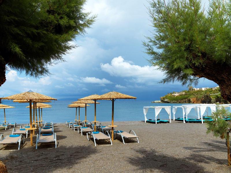 Plaża z leżakami, parasolami i białymi pawilonami nad spokojnym brzegiem pod zachmurzonym niebem.