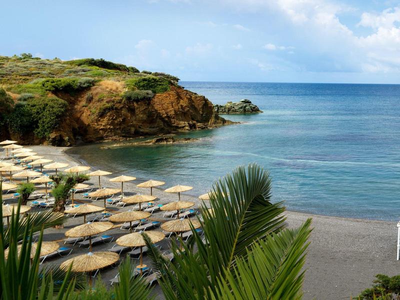 Plaża z parasolami i leżakami obok przejrzystego morza i skalistego wybrzeża przy słonecznej pogodzie