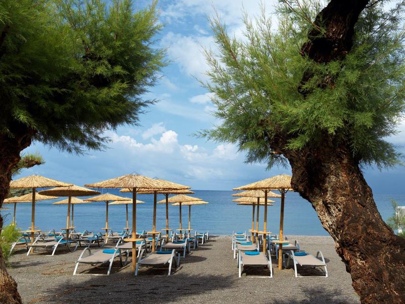 Plaża z leżakami i słomianymi parasolami nad spokojnym morzem pod niebieskim niebem.