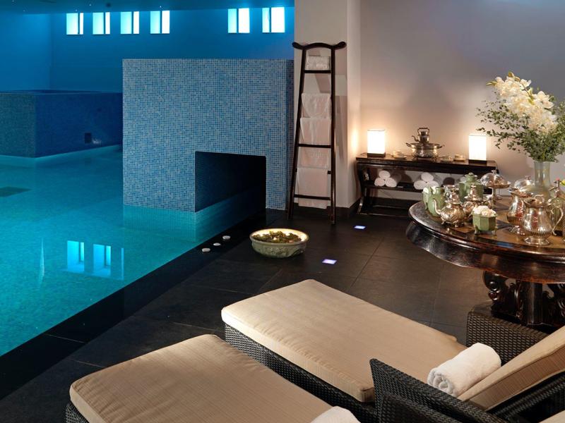 Elegancka strefa spa z niebieskim basenem, leżakami i dekoracyjnymi roślinami.