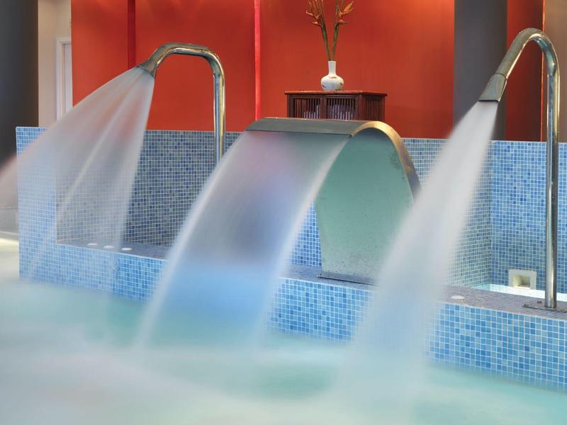 Nowoczesny basen kryty z wodospadami i czerwoną ścianą do relaksu.