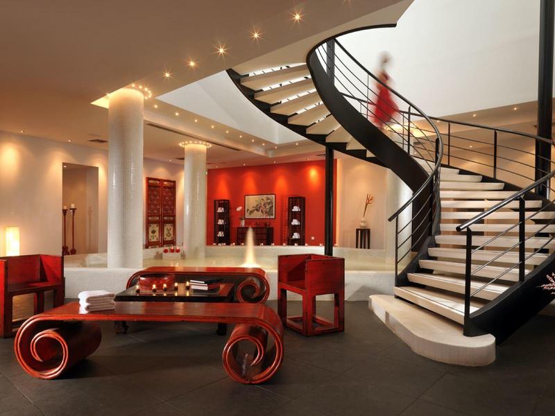 Elegancka lobby hotelowa z zakrzywionymi schodami, czerwonymi meblami i stylowym oświetleniem.