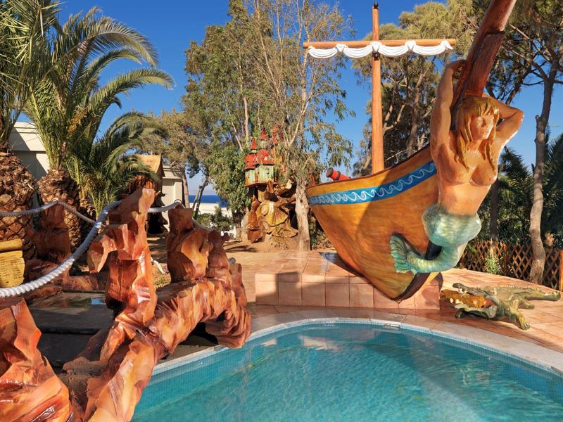 Kolorowy plac zabaw w kształcie statku pirackiego obok basenu w słonecznym otoczeniu.