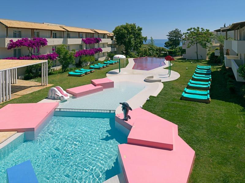 Nowoczesny basen hotelowy z różową obwódką, leżakami i widokiem na morze przy czystym niebie.