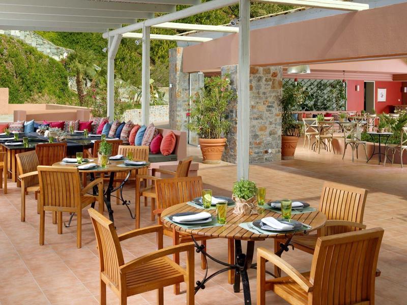 Taras restauracji z drewnianymi stołami, krzesłami i kolorowymi poduszkami w relaksującej atmosferze.