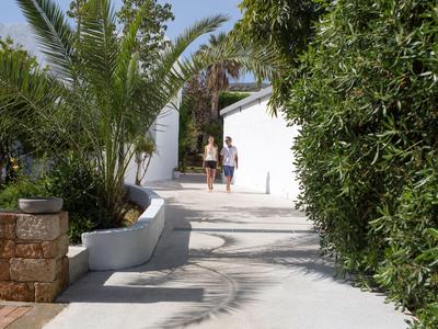 Camino con palmeras y setos que conduce a un edificio blanco, dos personas caminando por él.