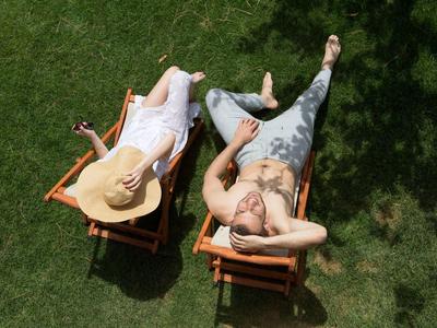 Due persone che si rilassano su sdraio sull'erba, una con cappello a tesa larga e l'altra con tatuaggi.