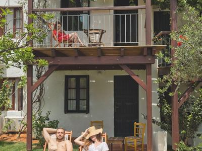Dos personas relajadas sentadas en sillas de jardín frente a una casa de dos pisos con balcón.