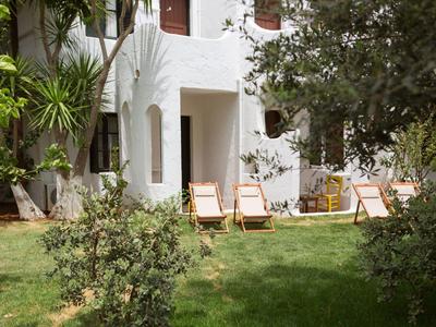 Edificio dell'hotel bianco con sedie a sdraio su prato verde circondato da alberi e piante.