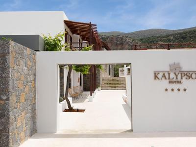 Entrada con puerta blanca al hotel Kalypso frente a montañas bajo cielo despejado.