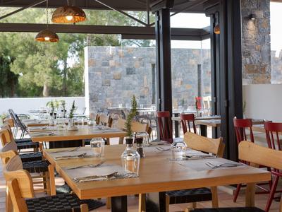 Ristorante accogliente con tavoli e sedie in legno e grandi finestre che mostrano il verde esterno.