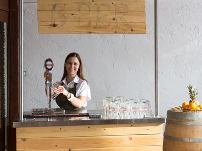 Barista versa una bevanda dietro un bancone di legno con bicchieri e frutta su una botte