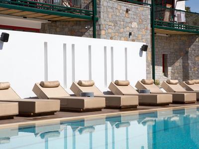 Fila de tumbonas beige junto a una piscina transparente con pared de piedra de fondo.