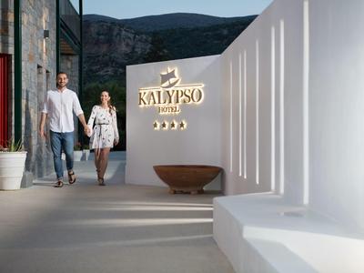 Coppia che cammina vicino al cartello dell'hotel Kalypso con architettura bianca moderna e vista sulla montagna.