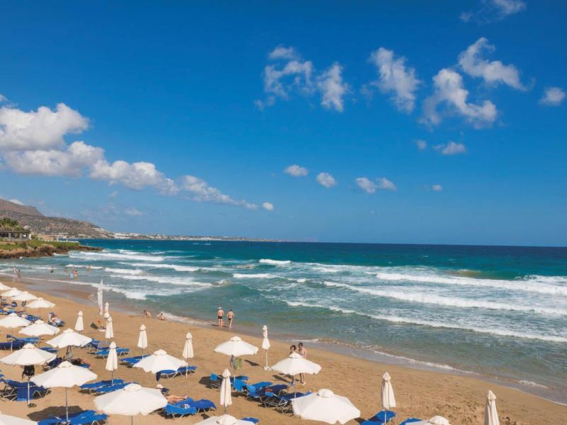 Spiaggia soleggiata con ombrelloni, lettini e onde sotto un cielo blu.