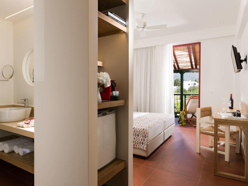 Camera d'hotel luminosa con letto, scrivania, TV e balcone con vista sul verde.