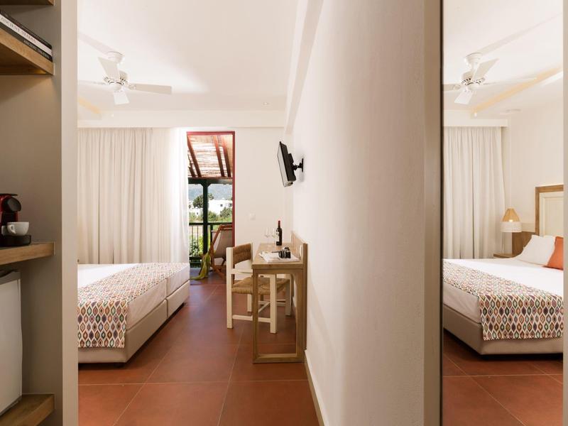 Camera d'hotel con letti singoli, mobili semplici e balcone.