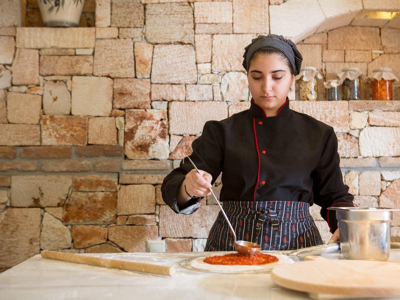 Cuochi in uniforme preparano pizza con salsa di pomodoro in cucina rustica.
