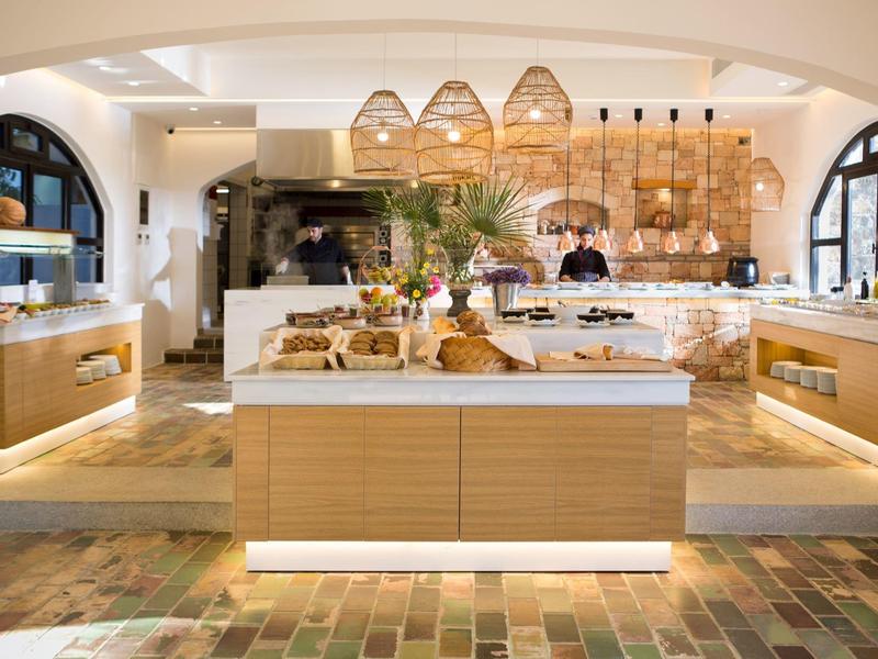 Area buffet luminosa in hotel con banconi in legno, pasticceria e lampade in vimini appese.