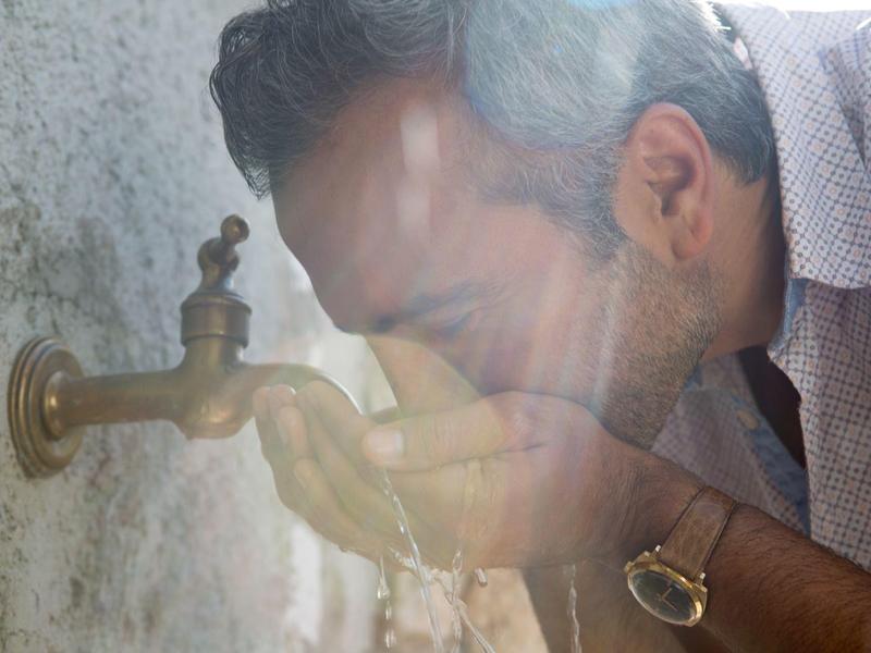 Uomo che si lava il viso con acqua da un rubinetto esterno alla luce calda del sole.