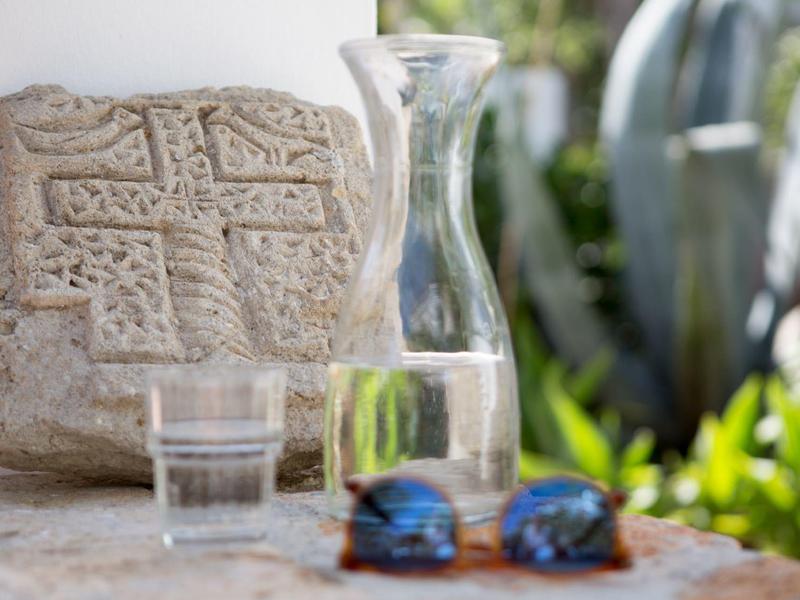 Pietra scolpita, caraffa in vetro, bicchiere d'acqua e occhiali da sole su un tavolo all'aperto soleggiato.