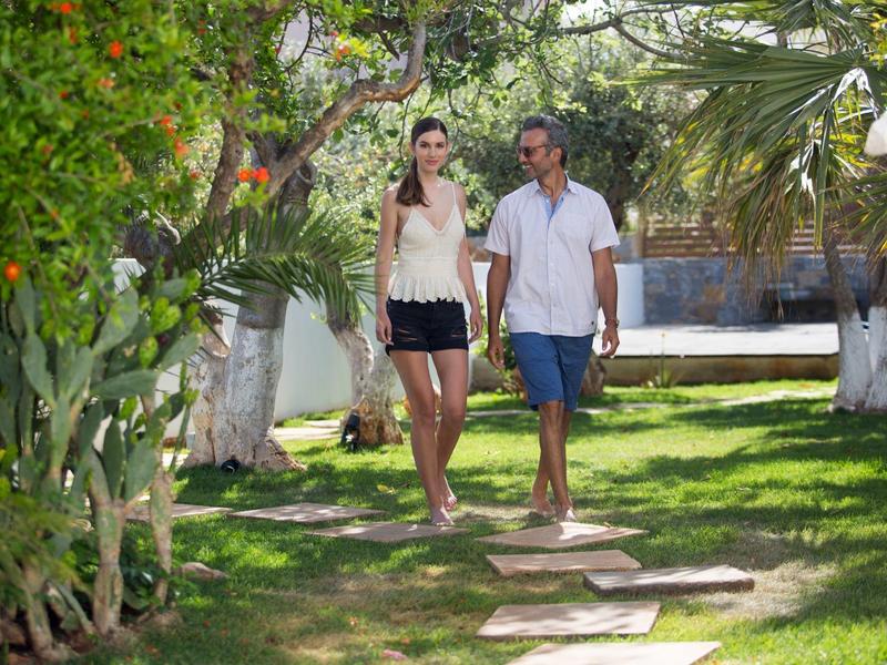 Una coppia cammina a piedi nudi su un sentiero di pietra in un giardino rigoglioso con erba verde e alberi.