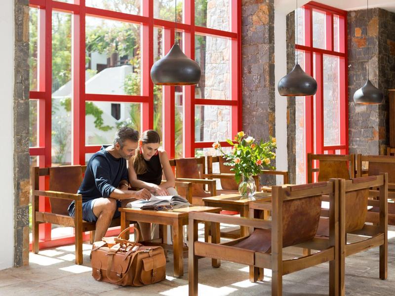 Due persone sedute a un tavolo di legno con grandi finestre con cornici rosse dietro di loro in una lounge luminosa.