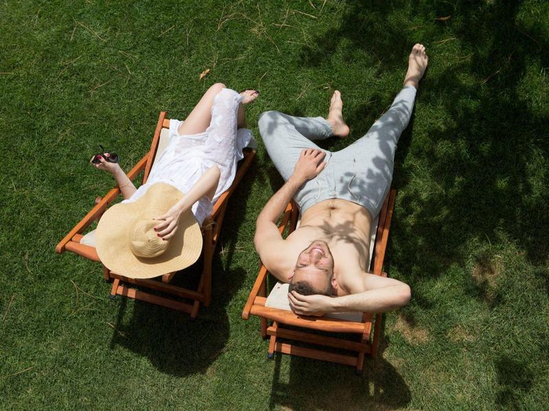 Due persone che si rilassano su sdraio sull'erba, una con cappello a tesa larga e l'altra con tatuaggi.