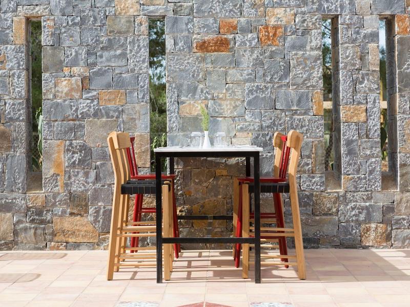 Tavolo all'aperto con sedie davanti a un muro di pietra al sole.