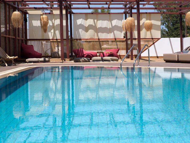 Piscina all'aperto con acqua blu circondata da lettini e area salotto ombreggiata